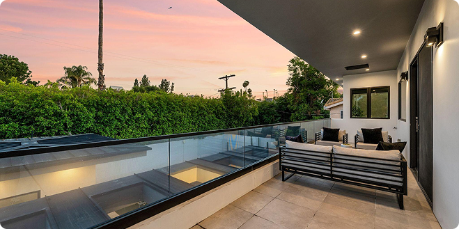 Modern rooftop terrace with outdoor seating, glass railing, and lush greenery at sunset